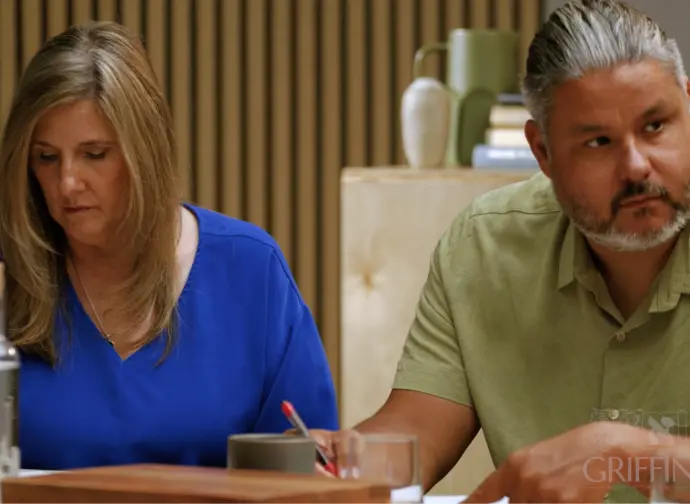 A man and woman sitting at a table, listening.